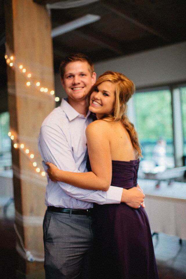 A man in a light dress shirt and a woman in a strapless purple dress smile and hug indoors, surrounded by string lights as they celebrate with fellow Service Professionals.