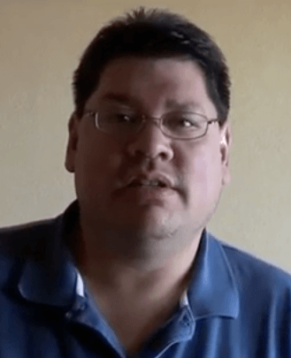 A man with short dark hair, glasses, and a blue polo shirt—dressed like many electricians and HVAC technicians—faces the camera against a plain beige background.