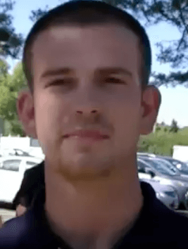 A man with short hair and a trimmed beard, possibly an electrician, stands outdoors in front of parked cars and trees. Active, direct version: A man who may be an electrician stands outside with his short hair and trimmed beard, positioned in front of parked cars and trees.