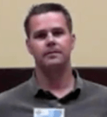 A man with short brown hair and a gray collared shirt stands indoors against a beige and dark brown background, representing skilled Service Professionals.