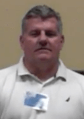 A middle-aged man with short gray hair stands against a plain beige background. He wears a white collared shirt and a name badge, representing skilled Service Professionals in the industry.