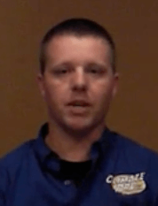 A person with short hair, wearing a blue collared shirt with a white logo, stands in front of a plain brown background. They represent skilled service professionals such as electricians and HVAC technicians.
