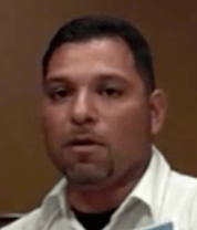 A man with short dark hair, a trimmed beard, and a mustache wears a white collared shirt and faces the camera against a plain brown background. He presents the professional appearance commonly seen among skilled service professionals such as electricians.