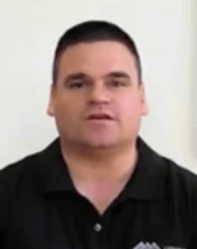 A man with short dark hair and a black collared shirt, dressed like an HVAC technician, faces the camera against a plain light background.