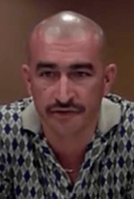 A man with a shaved head, mustache, and patterned shirt sits indoors against a plain background. He exudes the confident look of a seasoned service professional—like a plumber or electrician.