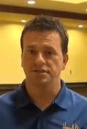 A man with short dark hair and a blue collared shirt stands indoors in front of a yellow wall. He looks like one of the skilled HVAC technicians ready to tackle any job.