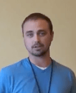 A man with short brown hair and a trimmed beard stands in front of a plain beige wall. He wears a blue shirt and a dark lanyard, projecting the look of one of the skilled Service Professionals.