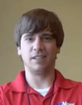 A plumber with straight brown hair and a red collared shirt stands indoors against a plain beige background.