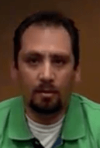 A man with short dark hair, a goatee, and a mustache wears a green shirt and looks directly at the camera with a neutral expression, displaying the confident demeanor of service professionals such as plumbers or electricians.