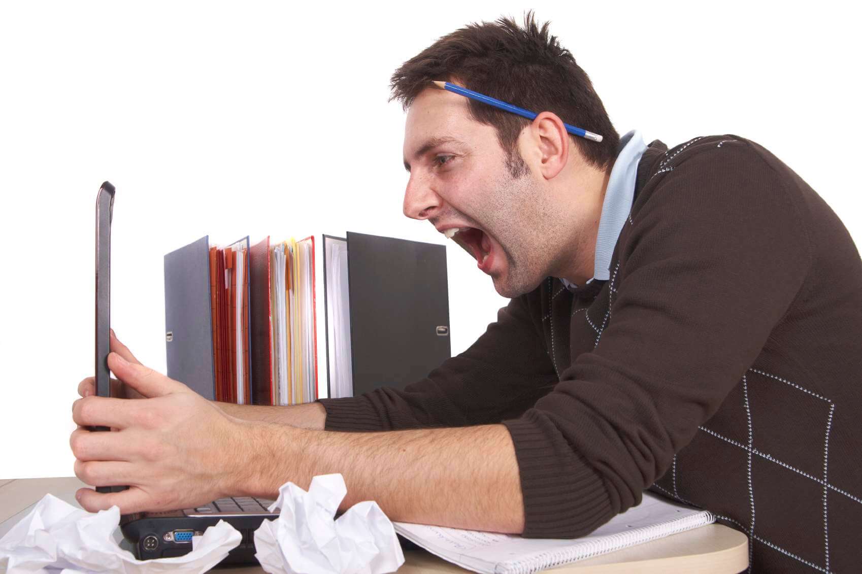 A man sits at a desk, surrounded by crumpled papers. He yells at his laptop. A pencil rests behind his ear, like an electrician's, and folders fill the background.