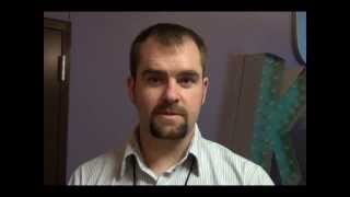A man with short hair and a goatee stands indoors, facing the camera. He wears a collared shirt and looks ready for work, like many Service Professionals or HVAC technicians. A large letter "K" dominates the background.