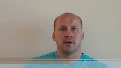 A man with a shaved head and a light blue shirt, resembling many skilled electricians, looks straight ahead against a plain, light-colored background.