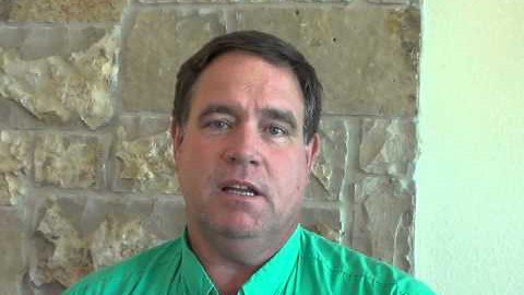 A man with short brown hair and a green collared shirt stands in front of a stone wall, looking directly at the camera. He is ready to assist you as one of the area's trusted service professionals.