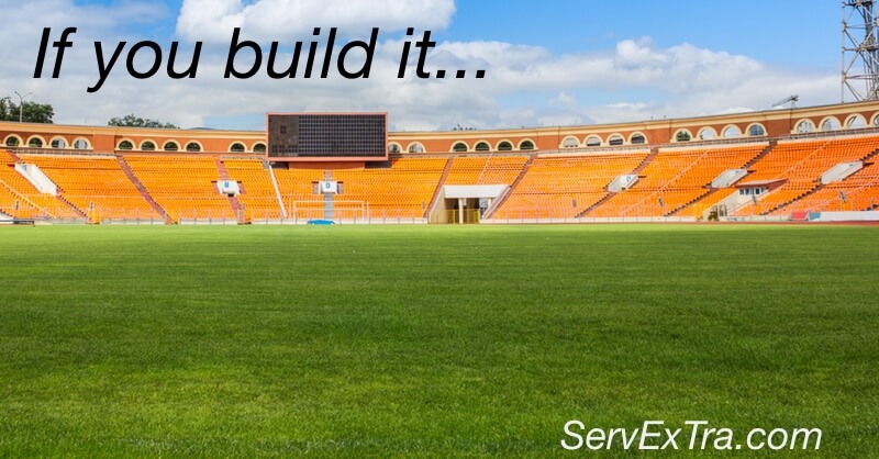 An empty stadium with orange seats and a green grass field displays the text: "Build it. Find your electrician or plumber at ServExTra.com.