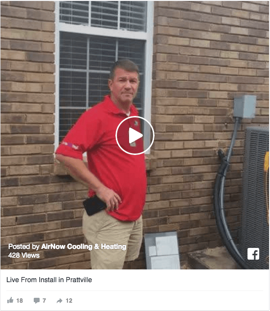 A man in a red shirt stands outside by a brick wall and an HVAC unit, holding his phone with a clipboard on the ground—an ideal scene for training or coaching home service business owners.