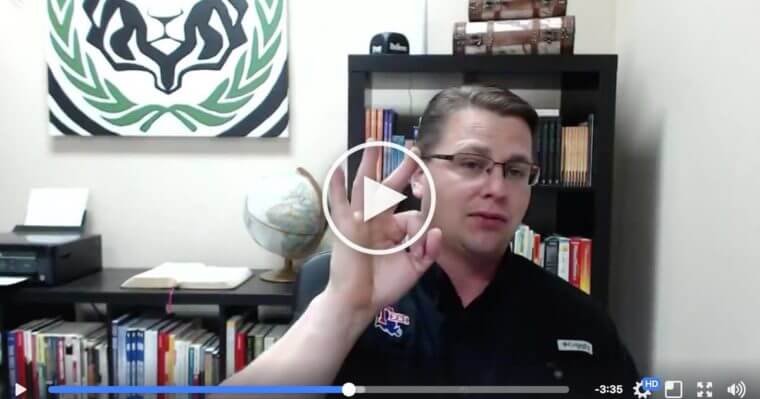 A man wearing glasses sits in an office and gestures with his right hand. Bookshelves, a globe, and a large emblem fill the space behind him, creating an inspiring setting for home service business owners seeking expert service training.