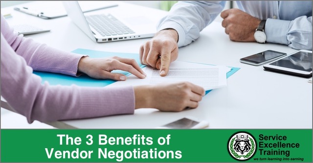 Two people sit at a desk, reviewing documents with laptops, a phone, and writing materials. They illustrate home service business owners discussing vendor negotiations and Service Excellence.