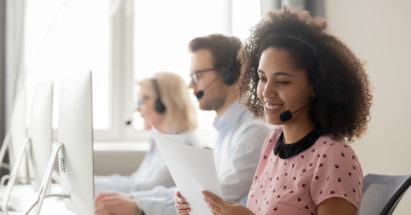 Smiling african american businesswoman call center operator agent wearing headset holding papers reading clients contacts working in customer service support helpdesk business office with colleagues