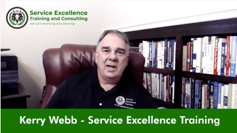 A man wearing a black "Service Excellence Training" shirt sits in front of a bookshelf, ready to coach home service business owners. The text "Kerry Webb - Service Excellence Training" appears at the bottom.