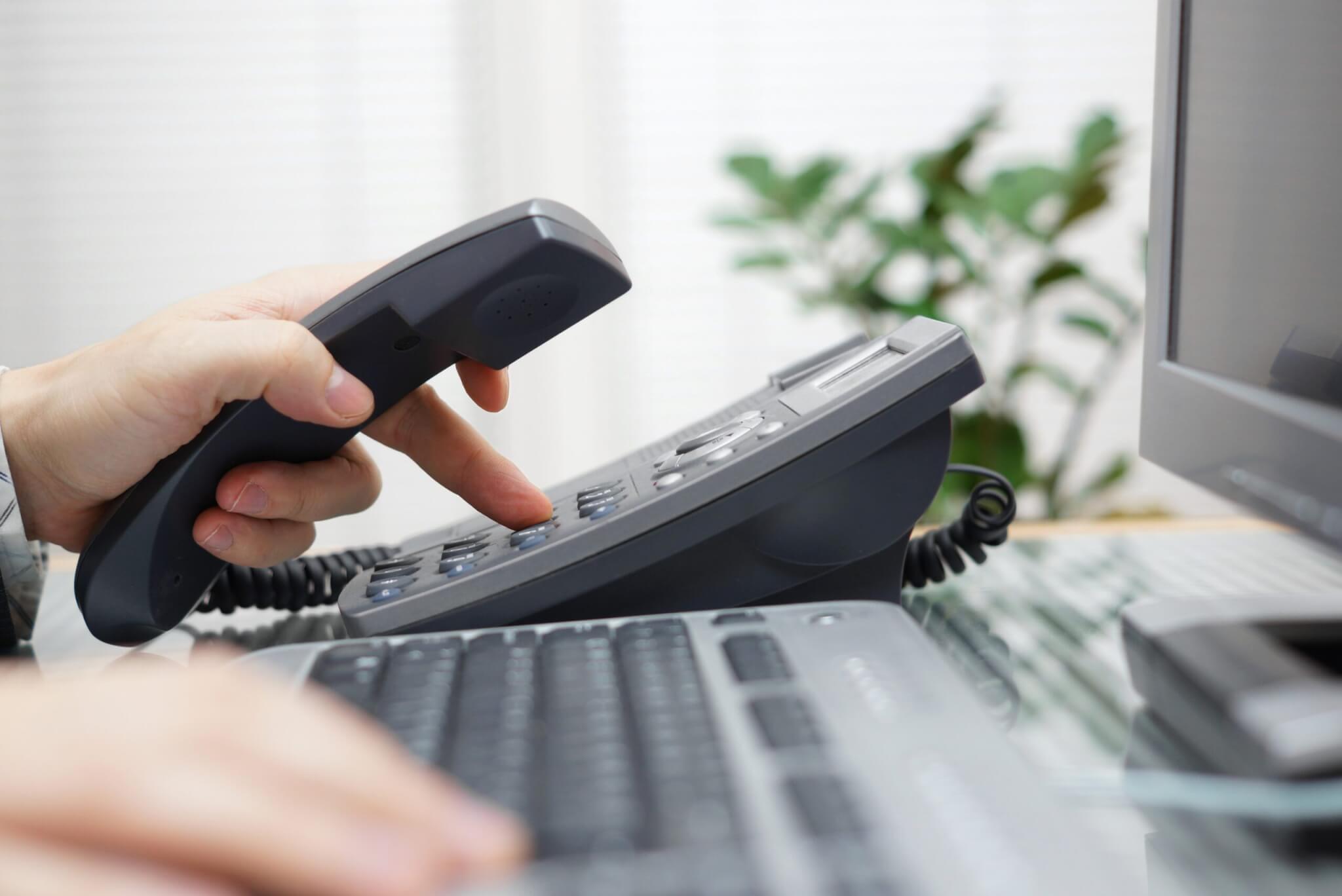 A person sits at a desk, uses a computer keyboard, and dials a number on the phone handset, demonstrating Service Excellence in managing home services.