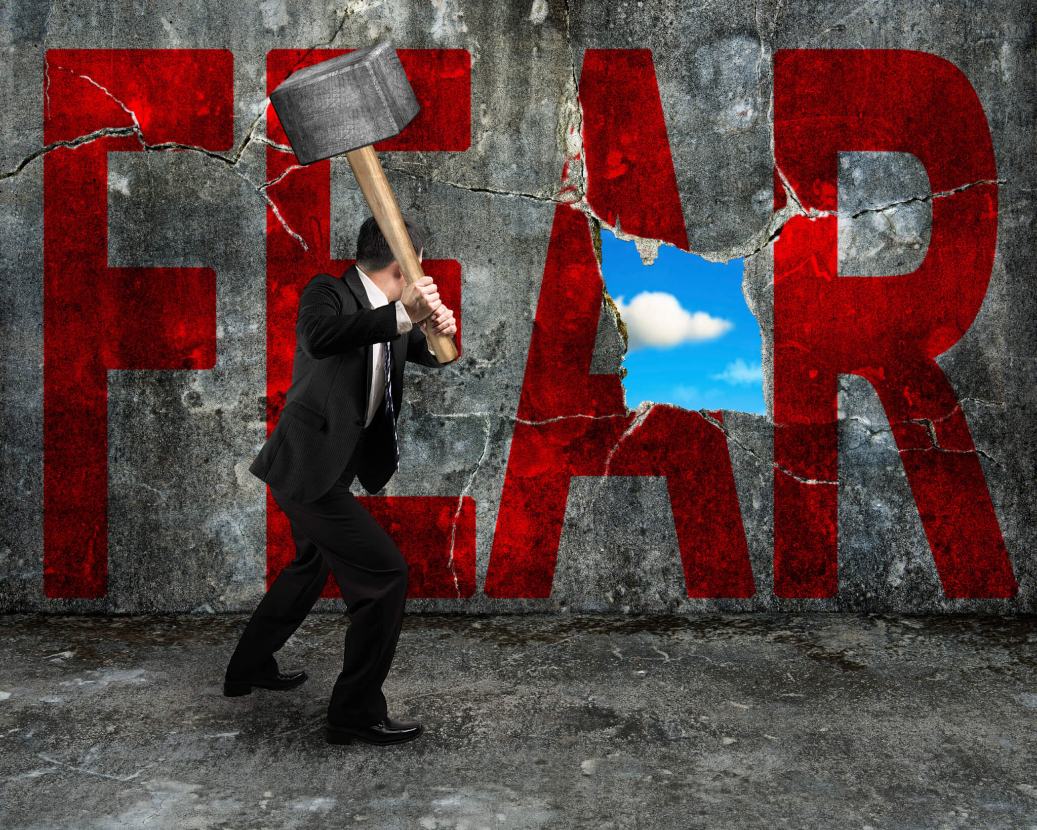 A person in a suit swings a sledgehammer, smashing through a cracked concrete wall labeled "FEAR." Blue sky and clouds appear through the opening, showing how coaching helps home service business owners break barriers.