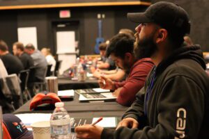 People sit at tables in a classroom, listen, and take notes during a Service Excellence training workshop.