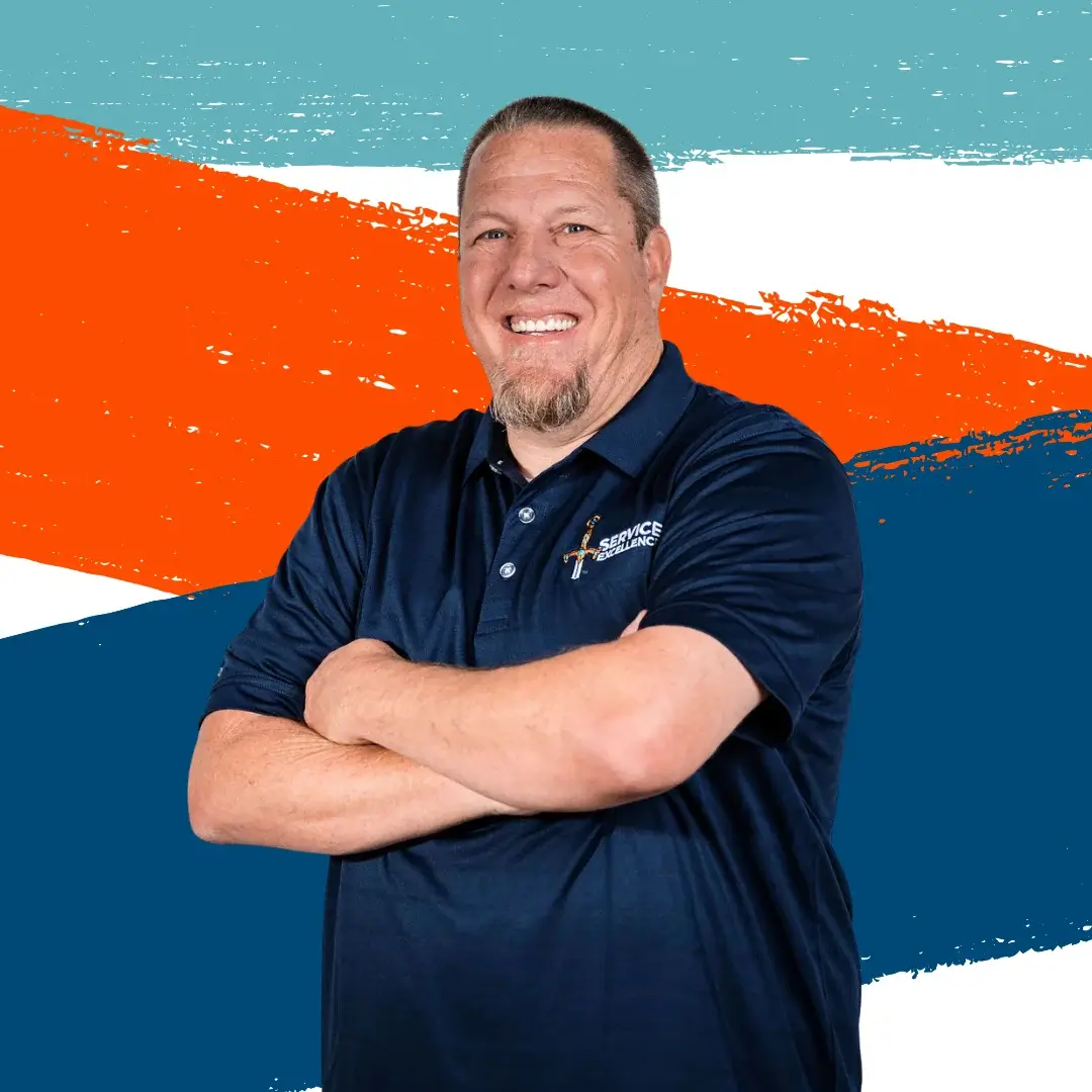 A short-haired man with a goatee crosses his arms and wears a navy blue polo shirt as he stands in front of a colorful abstract background. He is an expert in home services and service training.