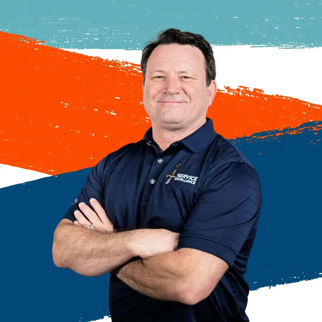 Chris Elmore stands with his arms crossed and smiles in front of teal, orange, and white painted stripes. His confident stance and expression reflect his commitment to Service Excellence in home services.
