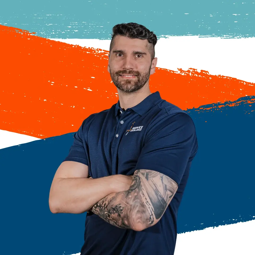 A bearded man with a tattooed forearm stands with his arms crossed, wearing a navy polo shirt in front of a colorful abstract background. He is ready to deliver expert training and coaching in home services.